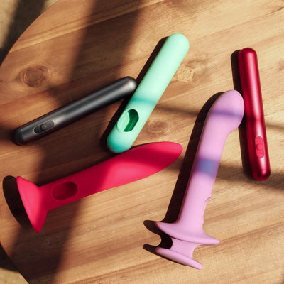Two cylinder shaped vibrators with circle caps and three silicone dildo sleeves on wooden table #pink
